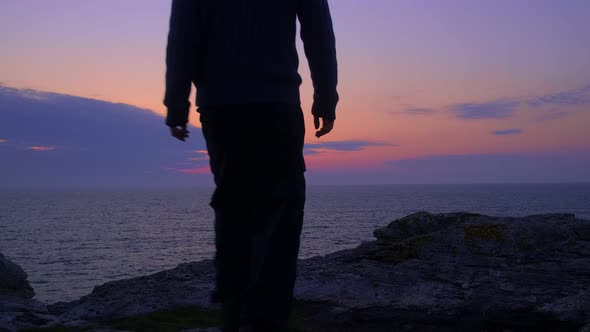 Young Man Walks to a Rocky Sea Shore to Wait for the Sunrise. Stands Upright. Silhouette