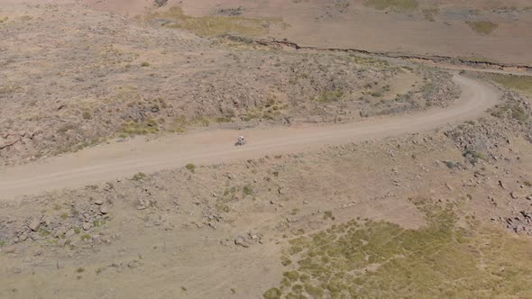 aerial shot following a mountain biker climbing up a pass on a gravel road