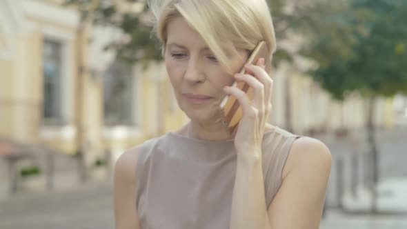 Close-up of Confident Mid-adult Caucasian Woman Walking Along City Street and Talking on the Phone