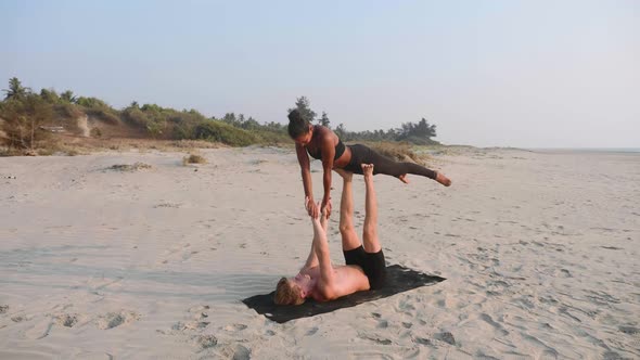 Fit Sporty Couple Practicing Acro Yoga with Partner Together on the Sandy Beach