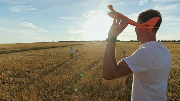 Man Flies Toy Red Plane Towards Small Sons in Mown Field