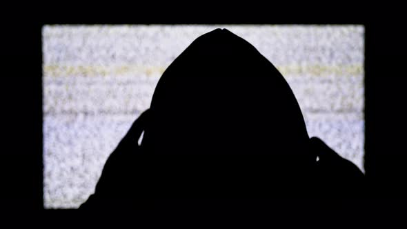 Silhouette of Man's Head in Hood Is Watching White Static Noise and TV Interference.