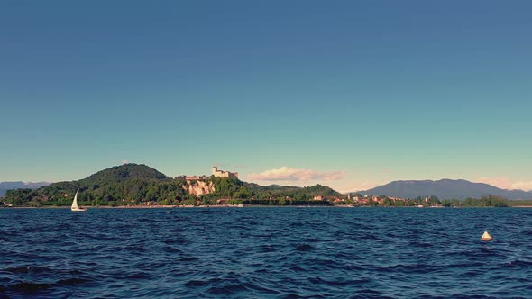 Small sailboat sailing on Maggiore lake agitated waters with mountains and Angera castle in backgrou