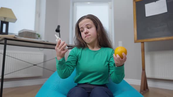 Embarrassed Little Person Choosing Medications Vs Organic Orange Sitting on Bag Chair Indoors