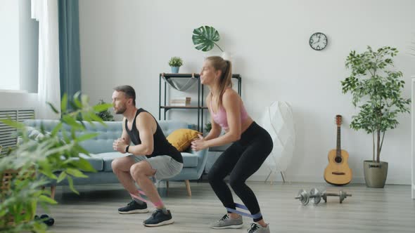 Beautiful Young Couple Exercising with Resistance Bands Squatting and Raising Legs Working Out at