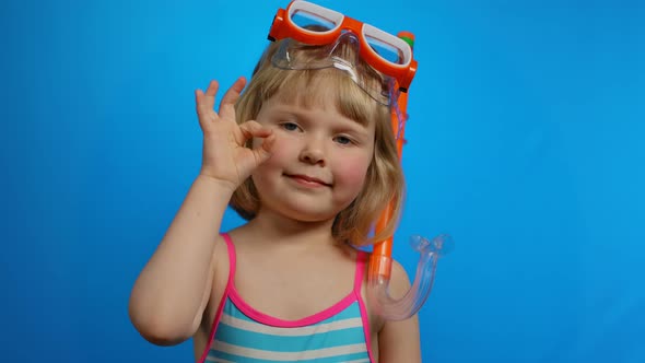 Little Blond Girl with Short Hair in a Swimsuit Shows Ok Gesture in the Studio