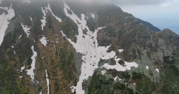 view on zig zag mountain trail with snow on slope, aerial drone shot