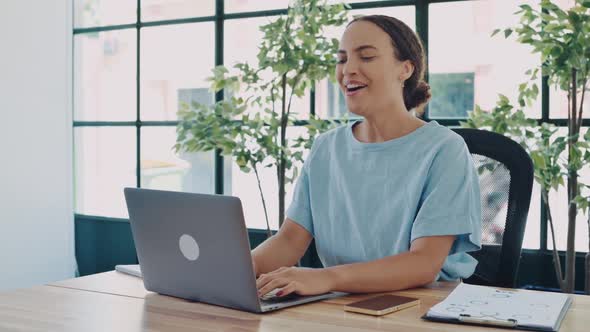 Joyful Amazed Happy Brazilian or Hispanic Young Business Woman Sitting at a Desk with a Laptop in