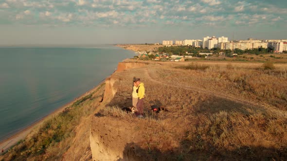 Happy Couple with Dog Standing on Edge of Cliff and Enjoying Amazing View Above Sea Water