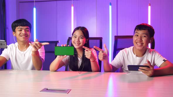 Team Of Asian Gamers Sitting On Chair And Pointing To Mock Up Green Screen Mobile Phone