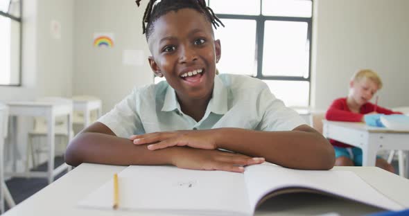 Video of happy african american boy sitting at school desk