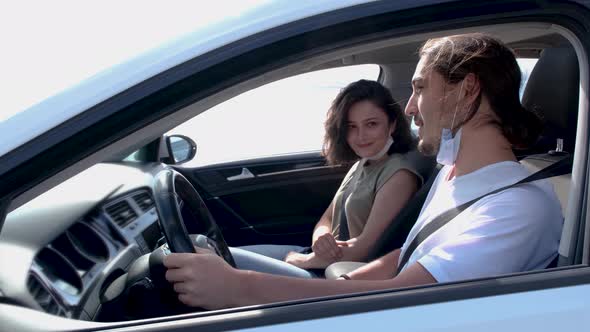 Happy young couple, friends with face masks sitting in the car and talking each other.