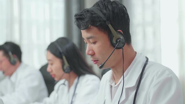 Asian Man Doctor With Colleagues Working As Call Centre Agent Speaking To Customer