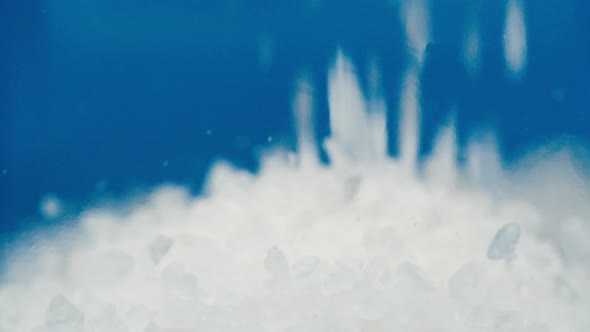 Closeup of Falling Down Salt Into Glass Jar on Blue Background