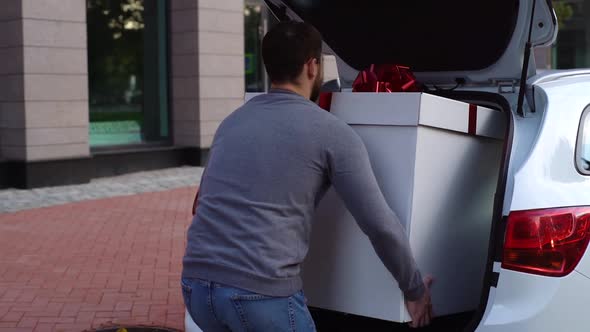 Back view of delivery man takes out large festive white box