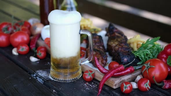 Pouring Beer Into Glass Mug with Delicious Beef or Pork Frying Ribs on Background