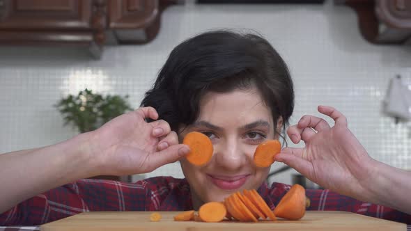 Portrait of Laughing and Smiling Girl Putting in Front of the Eyes Orange Slices of Carrot