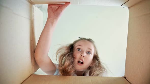 Beautiful Small Girl with Blonde Hair Opens Carton Package Showing Joy and Surprise on Her Face