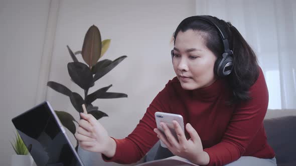 Asian woman on redshirt using a tablet with headphone for meeting online at home