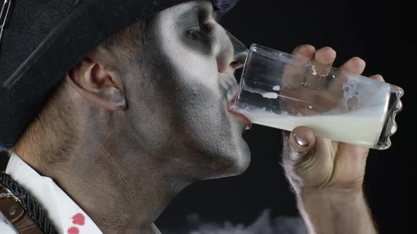 Creepy Man with Skeleton Makeup in White Shirt. Guy Looking at Camera, Drinks Milk From a Glass