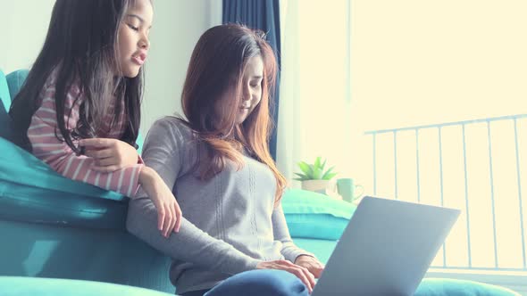 asian single mother working with laptop at home in living room with her daughter