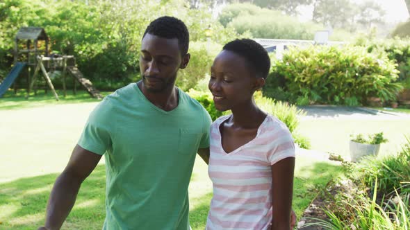 Smiling african american couple taking selfie with smartphone embracing in sunny garden