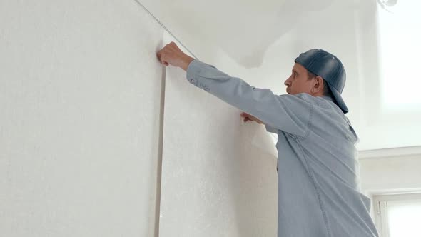 Man Applying a Roll of Wallpaper to the Wall Smoothes Pasted Wallpaper