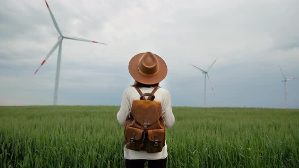 Young woman in a hat and with a backpack in a field with windmills