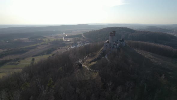 A tracking aerial drone shot of the Chęciny Royal Castle revealing the landscape of the valley. This