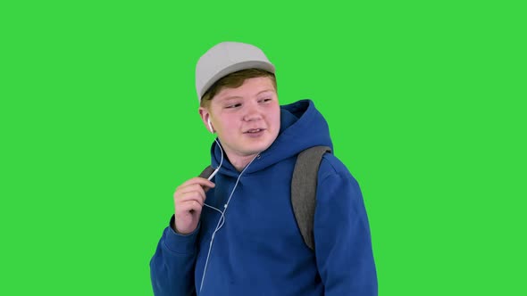 Teenager Boy Calling on Mobile Phone Using Handsfree While Walking on a Green Screen Chroma Key