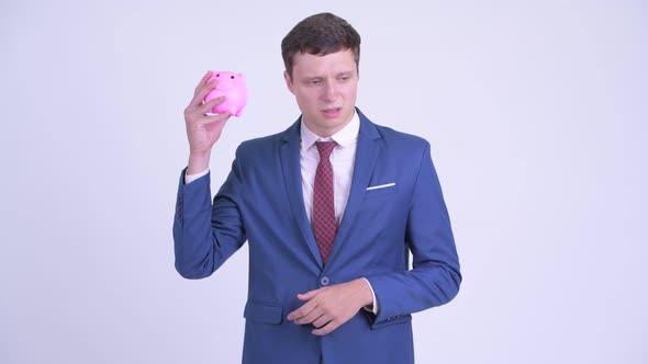 Stressed Young Businessman Holding Piggy Bank and Giving Thumbs Down
