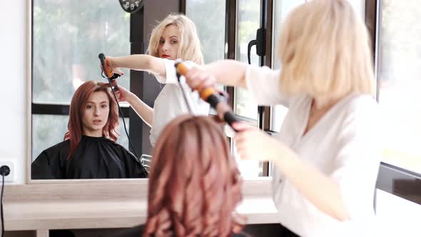 Stylist Curling Girl's Hair in Modern Beauty Studio
