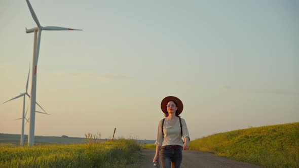 Attractive woman with a camera walking near a field with alternative green energy windmills