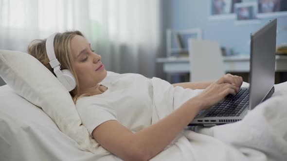 Smiling Girl Lying in Bed, Communicating With Friends in Social Media on Laptop