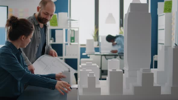 Man and Woman Working Together to Design Blueprints Plan Looking at Building Model