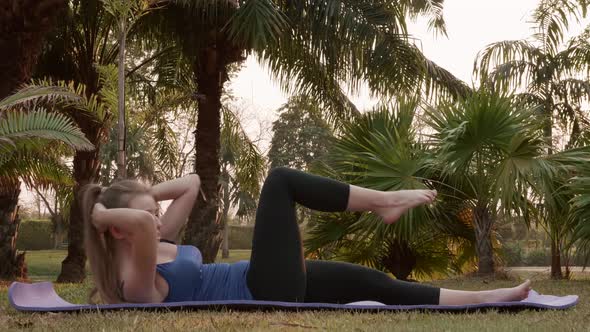 Beginning Fitness Woman is Pumping ABS Exercise on Yoga Mat in Public Park