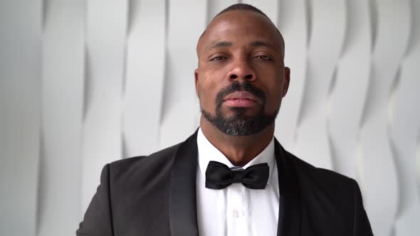 Portrait of an African Man with a Beard in a Tuxedo and a Bow Tie. He Stands Against the White Wall