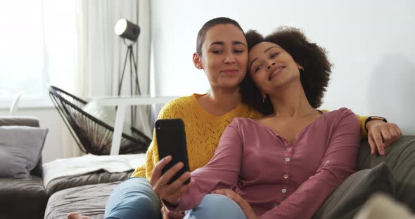 Lesbian couple using mobile phone and taking picture in living room