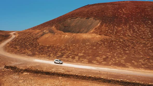 White Car Driving Alone Travel on Empty Dirt Road Freeway Through Desert Volcanic Landscape at