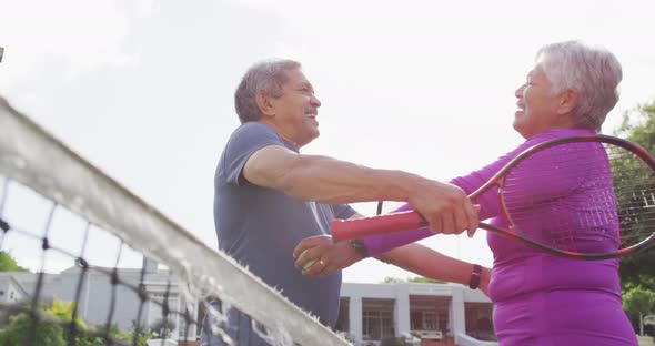 Video of happy biracial senior couple embracing on tennis court