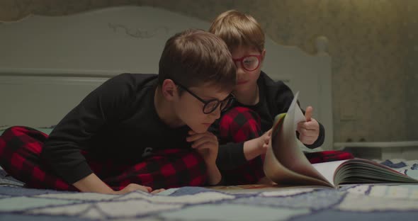 Two Kids in Eye Glasses and the Same Pajamas Reading Book at the Bedtime