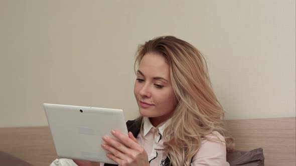 Smiling Nice Young Woman Uses a Digital Tablet Doing On-line Shopping Sitting on a Bed at Home