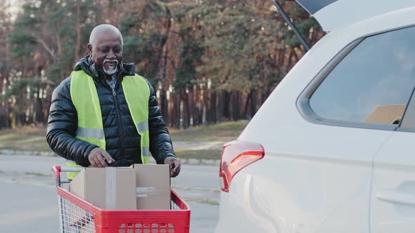 Elderly African American Man Store Worker Hauling Cart with Cardboard Boxes to Car Old Handyman