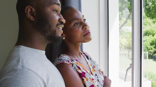 African american couple talking to each other while looking out of the window at home