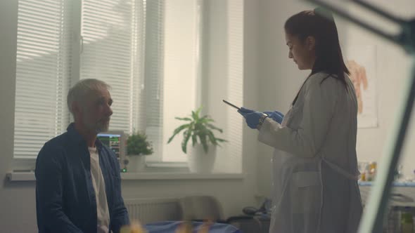 Doctor Consulting Sick Senior Patient Using Tablet in Hospital