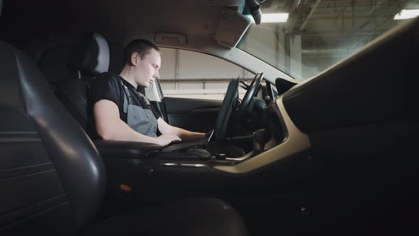 A Man is a Mechanic Sitting in the Car and Doing Computer Diagnostics of the Engine and Systems