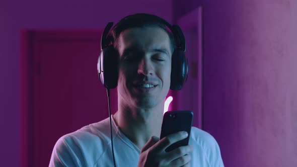 Portrait of Smiling Man Enjoys Listening To Music with Headphones in Neon Light. Young Male