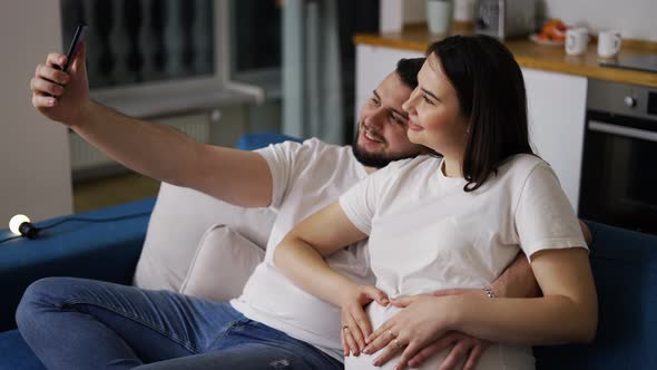 Happy Man and His Pregnant Wife Taking Selfie By Smartphone at Home