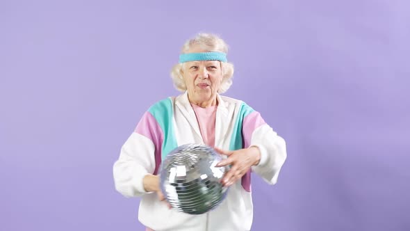 Happy Senior Woman in White Sportswear Holding Discoball in Hands on Purple