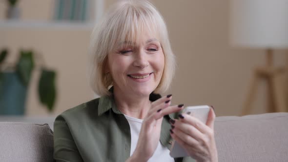 Mature Elderly Mature 60s Caucasian Woman with Phone Female Smiling Uses Mobile App at Home Buys